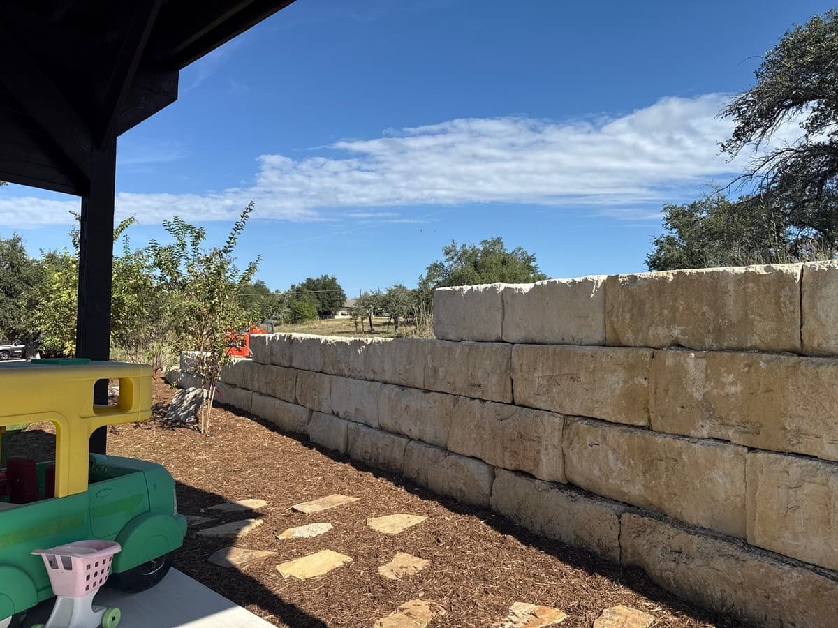Dry-stack wall construction detail showing base trench, crushed stone footing, block offset, and cap placement
