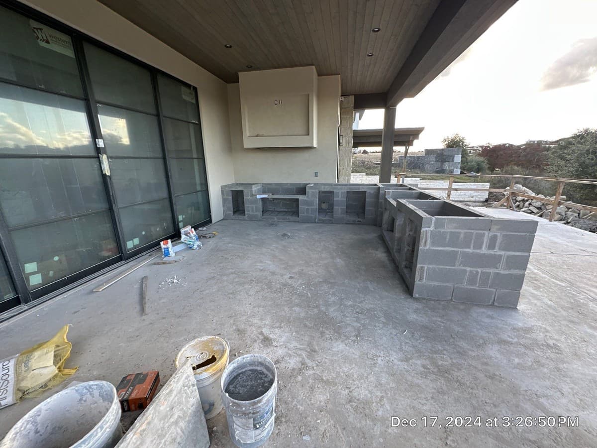 Outdoor kitchen construction sequence: steel frame, cement board substrate, stone veneer, and appliance rough-in